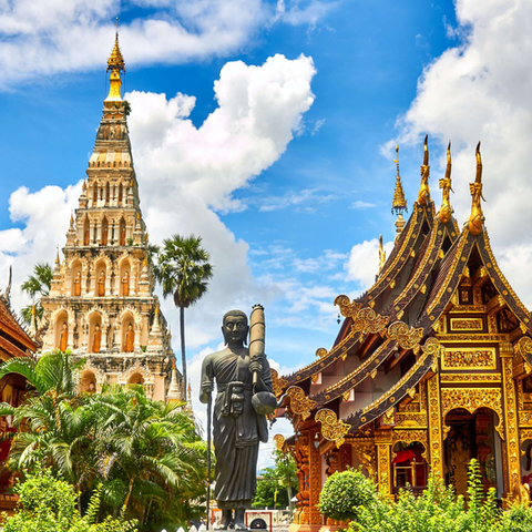 Golden Buddhist temple and Buddha statue among palm trees