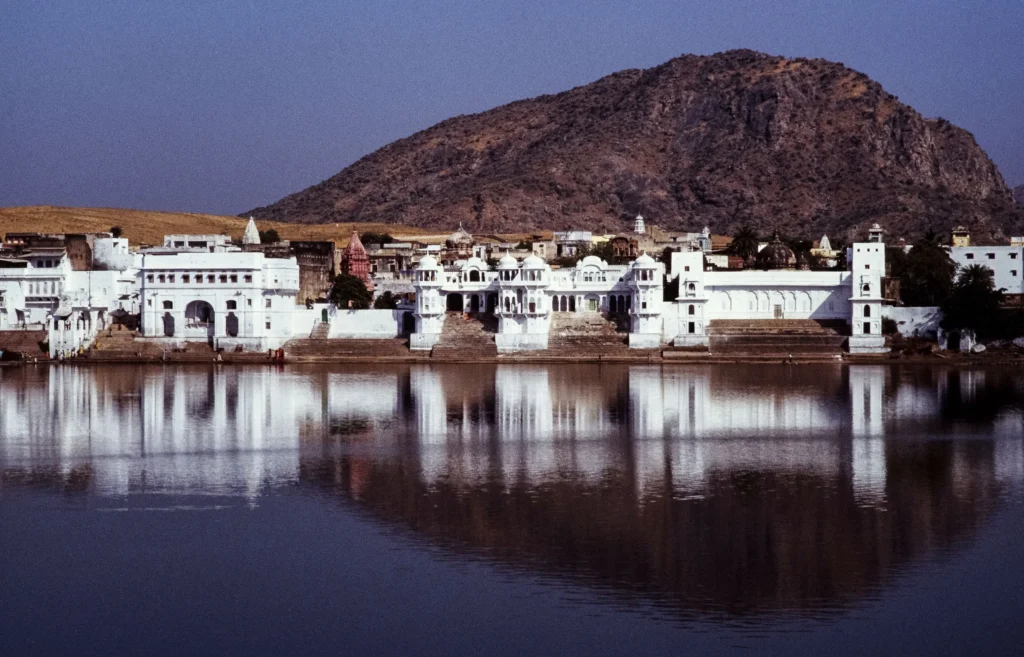 White ghats and temples of Pushkar mirrored in the lake, hill behind