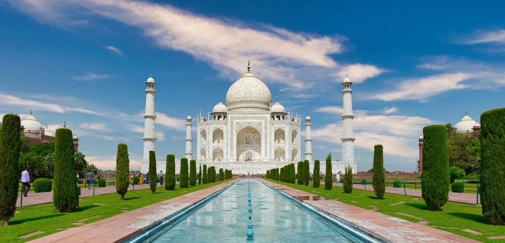 Taj Mahal beyond its long reflecting pool and cypress rows under blue sky