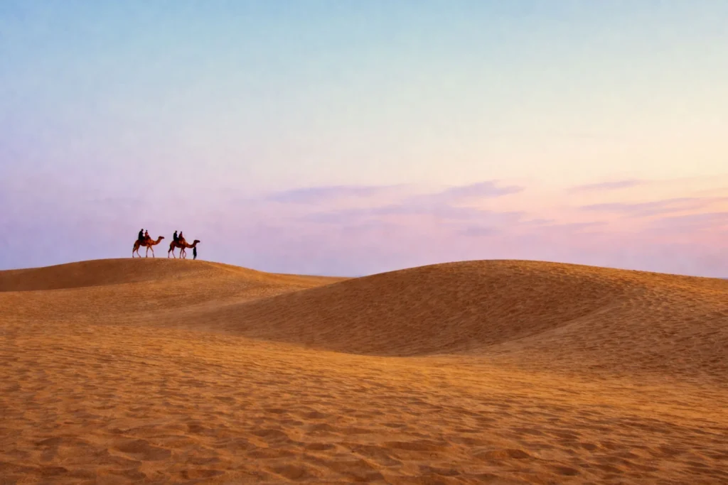 Two camels with riders crossing golden Thar Desert dunes at dusk