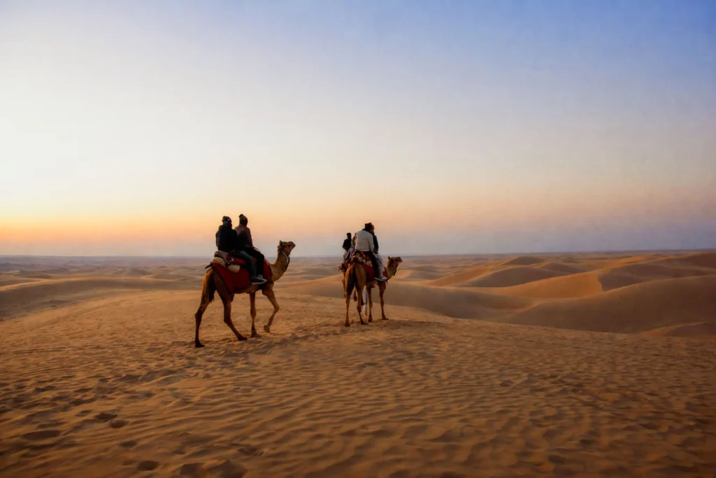 Camel riders crossing the sand dunes near Jaisalmer at sunset