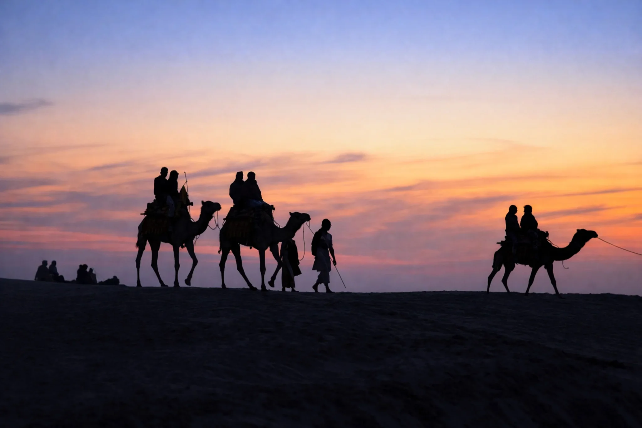 Silhouetted camel caravan against an orange desert sunset