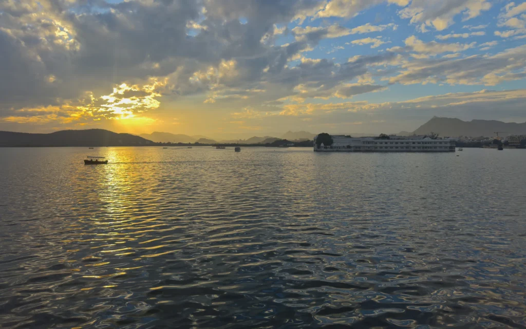 Sun setting through clouds over Lake Pichola, the Lake Palace on the right