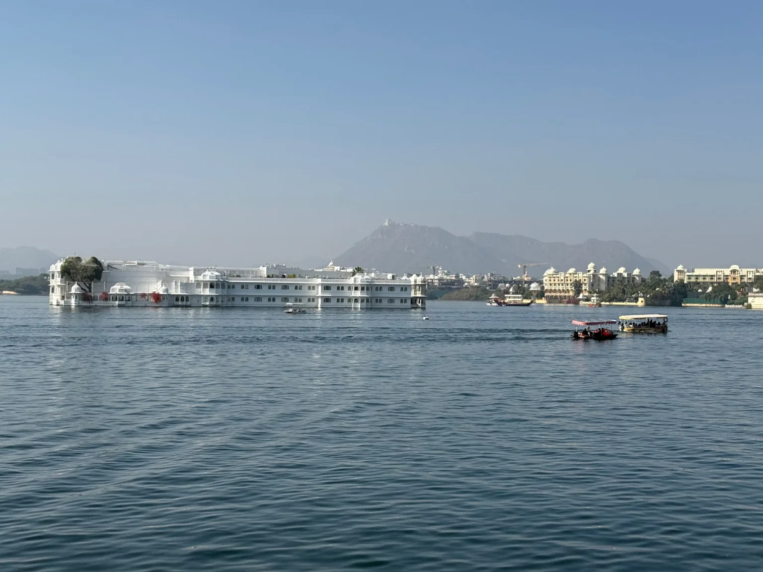 Taj Lake Palace on Lake Pichola with boats and distant hills