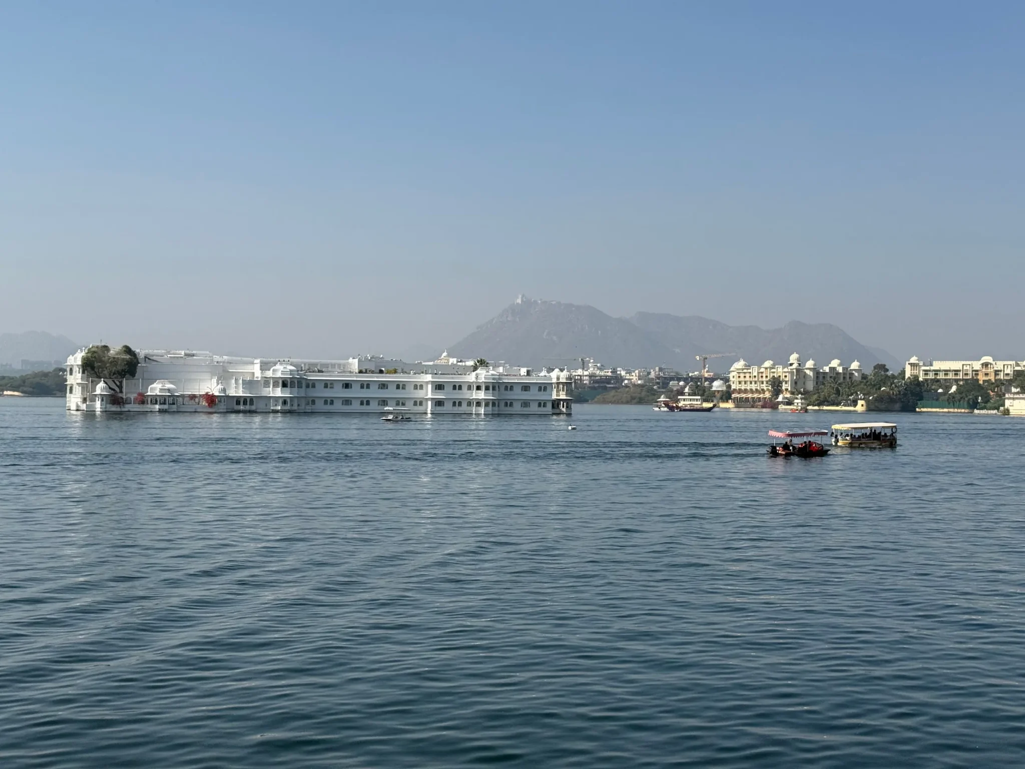 Taj Lake Palace on Lake Pichola with boats and distant hills